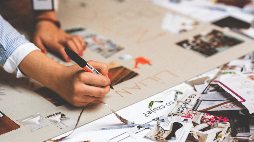 Photo d'une personne (on ne voit que sa main) qui dessine et colle des éléments sur une fresque en papier