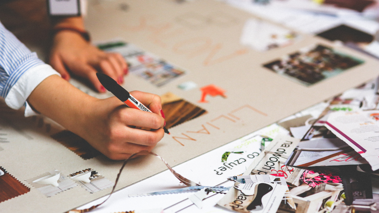 Photo d'une personne (on ne voit que sa main) qui dessine et colle des éléments sur une fresque en papier